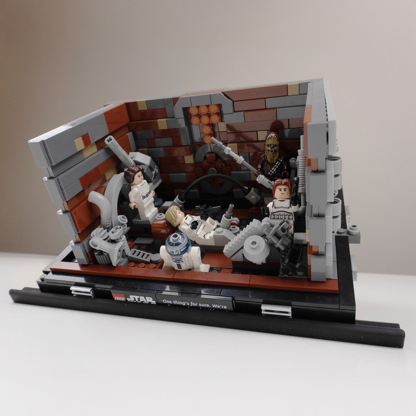 A LEGO diorama depicting a scene from Star Wars, featuring minifigures of characters like Luke Skywalker, Princess Leia, Han Solo, Chewbacca, and R2-D2 in a mechanical room setting.